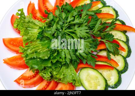 Tomaten, Gurken, Paprika in Scheiben geschnitten und mit Petersilie und Salat garniert. Teller Mit Frischem Gemüse. Isolieren Stockfoto