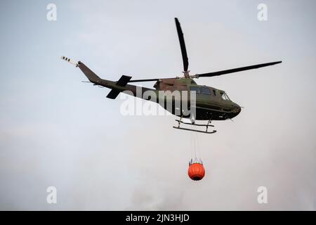 Waldbrandbekämpfung im Wald mit einem Hubschrauber, der einen Wassereimer trägt Stockfoto