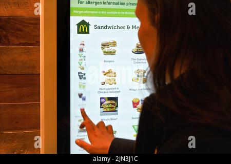 London, Großbritannien - 01. Februar 2019: Frau, die in einer der McDonalds-Filialen Lebensmittel auf einem großen Touchscreen bestellt, Nahaufnahme von hinten Stockfoto