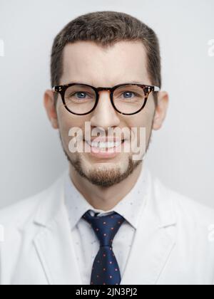 Porträt eines glücklichen jungen bärtigen männlichen Arztes, der mit einer Brille lächelt, die auf weißem Hintergrund isoliert ist Stockfoto