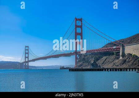Blick auf die Golden Gate Bridge während des Tages in San Francisco, Kalifornien. Es gibt einen Bootssteg gegen den Berg auf der rechten Seite und einen Blick auf die Berge Stockfoto