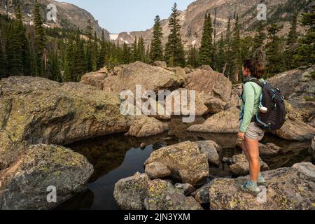 Woman steht in Rocks, umgeben von Cool Waters, am Ufer des Lake Haiyaha im Rocky Mountain National Park Stockfoto