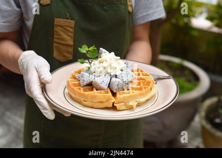 Frau hält belgische Waffeln mit Drachenfrucht und Eis auf einem Teller Stockfoto