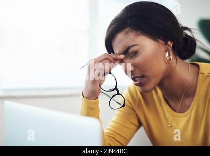 Diese Kopfschmerzen kamen aus dem nichts. Eine attraktive junge Frau, die allein zu Hause saß und unter Kopfschmerzen litt, während sie ihren Laptop benutzte. Stockfoto