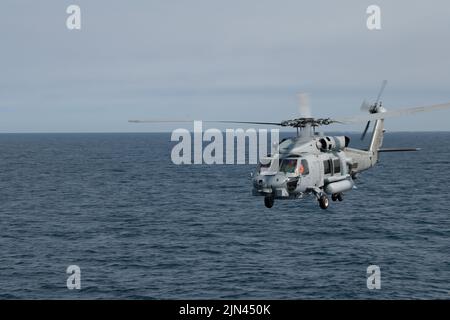 Ein Helikopterpilot der Royal Danish Navy MH-60R, der an HDMS Triton angeschlossen war, waves, als er während der Operation Nanook 2022, Northern Atlantic Ocean, am 5. August 2022, an der Hafenseite des USCGC Bear (WMEC 901) vorbeifliegt. Die Operation Nanook ist eine multinationale militärische Übung, die die Fähigkeiten der Vereinigten Staaten und der Partnerländer hervorhebt, gemeinsame maritime Ziele in arktischem Umfeld voranzutreiben. (USA Foto der Küstenwache von Petty Officer, Klasse 3., Matthew Abban) Stockfoto