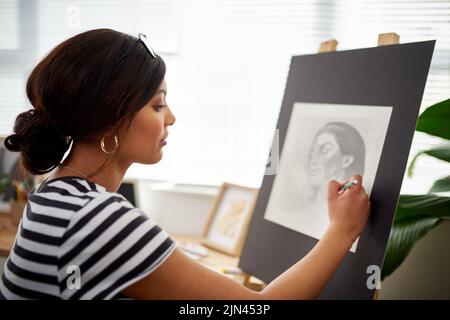 Liebe zum Detail ist das Geheimnis. Eine attraktive junge Künstlerin zeichnet ein Porträt einer Frau in ihrem Atelier. Stockfoto