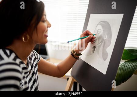Dieses Bild kommt genau so heraus, wie ich es mir vorgestellt habe. Eine attraktive junge Künstlerin, die ein Porträt einer Frau in ihrem Atelier zeichnet. Stockfoto
