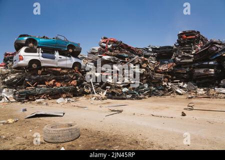 Gestapelte und zerdrückte, weggeworfene Autos auf dem Schrott-Recyclingplatz. Stockfoto