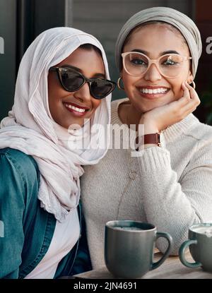 Hatten so eine gute Zeit. Beschnittenes Porträt zweier anhänglicher junger Freundinnen, die in Hijab gekleidet in einem Café zusammen Kaffee trinken. Stockfoto
