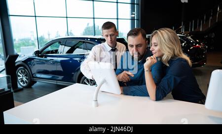 Kaukasisches Ehepaar wählt ein Auto in einem Autohaus auf digitalen Tablets. Stockfoto