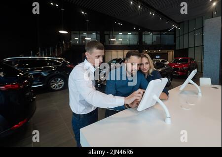 Kaukasisches Ehepaar wählt ein Auto in einem Autohaus auf digitalen Tablets. Stockfoto