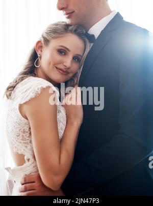 Together Forever ist ein wunderschöner Ort. Ein beschnittenes Porträt einer attraktiven jungen Braut, die drinnen steht und ihren frisch vermählten Ehemann umarmt. Stockfoto