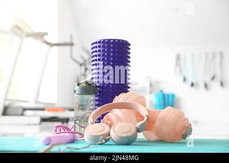 Schaumstoffrolle mit Kopfhörern, Hanteln, Flasche und Springseil auf Matte im Fitnessstudio Stockfoto