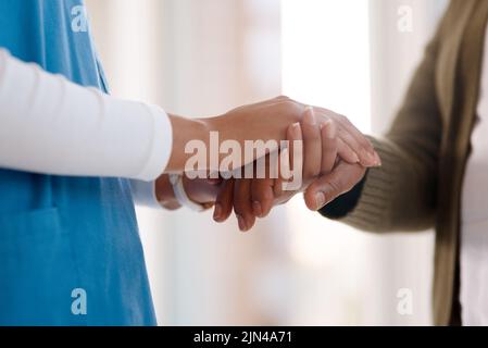 Sie können meine Hand für Unterstützung halten, wann immer Sie benötigen. Nahaufnahme einer nicht erkennbaren Krankenschwester, die eine ältere Frau in der Hand hält. Stockfoto