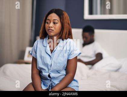 Sie weiß nicht, was sie tun soll. Eine attraktive junge Frau, die deprimiert aussahe, während sie mit ihrem Mann im Hintergrund auf dem Bettrand saß. Stockfoto