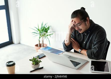 Diese Kopfschmerzen machen die Sache nur noch schlimmer. Ein hübscher junger Geschäftsmann, der gestresst aussieht und am Arbeitsplatz unter Kopfschmerzen leidet. Stockfoto