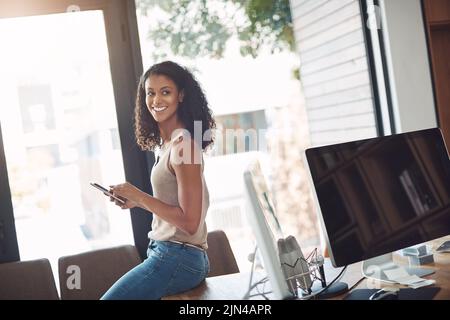 Legere Frau, die in einem Heimbüro ein Telefon hält, genießt es, an ihrem Schreibtisch ferngesteuert zu arbeiten. Ehrlicher, echter und authentischer Moment des digitalen Marketings Stockfoto