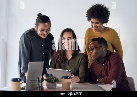 Es braucht das wahre Herz eines Teams, um zu gewinnen. Eine vielfältige Gruppe von Geschäftsleuten, die gemeinsam im Büro an einem Tablet arbeiten. Stockfoto
