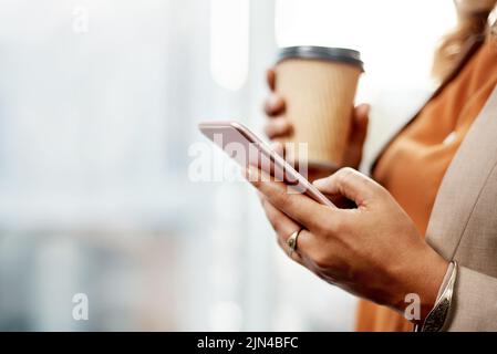 Treffen wir uns nach der Arbeit. Eine unkenntliche Geschäftsfrau, die Kaffee trinkt und in ihrem Büro ein Mobiltelefon benutzt. Stockfoto