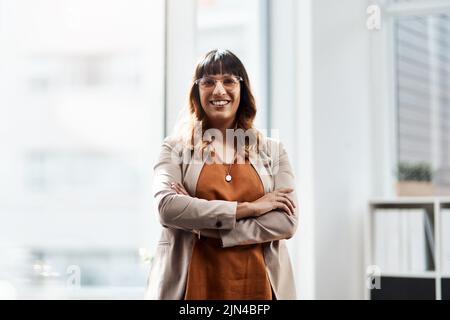 Shes war immer ein Go-Getter. Porträt einer attraktiven jungen Geschäftsfrau, die mit gefalteten Armen in ihrem Büro posiert. Stockfoto