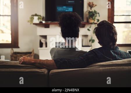 Ein Paar, das zusammenfließt, bleibt zusammen. Rückansicht eines jungen Paares, das zu Hause auf dem Sofa sitzt und gemeinsam fernsieht. Stockfoto