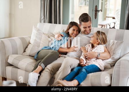 Ich liebe es, meine Mädchen glücklich zu sehen. Ein entzückendes kleines Mädchen verbringt viel Zeit mit ihren Eltern auf dem Sofa zu Hause. Stockfoto