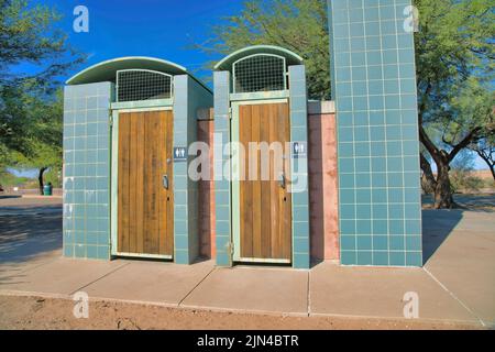 Öffentliche Toiletten für Männer und Frauen im Sweetwater Wetlands in Tucson, Arizona. Zwei öffentliche Toiletten mit Holztüren und Schilder an gefliesten Wänden Stockfoto