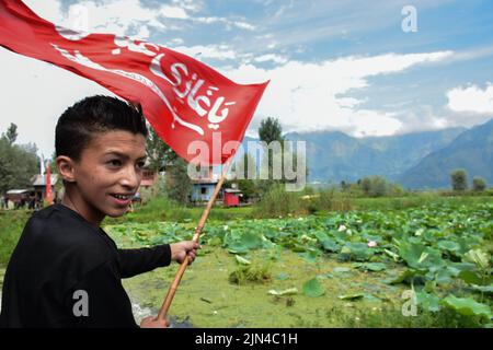 Srinagar, Indien. 08. August 2022. Ein Kashmiri-schiitischer Trauerling hält während einer religiösen Prozession in den Innenräumen des Dal-Sees in Srinagar eine religiöse Flagge. Muharram ist ein Monat der Trauer zum Gedenken an das Martyrium von Imam Hussain, dem Enkel des Propheten Muhammad (PBUH). Kredit: SOPA Images Limited/Alamy Live Nachrichten Stockfoto