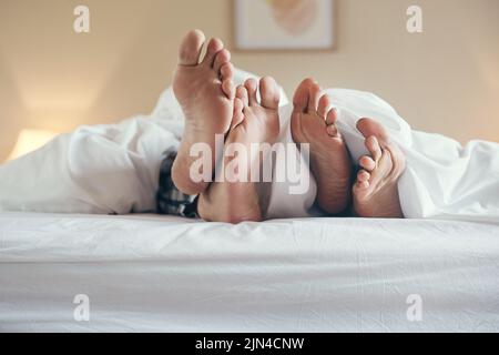 Heute sind wir nicht mehr aus dem Bett gekommen, ein nicht erkennbares Paar hat die Füße unter die Laken gestochen, während es zu Hause zusammen im Bett lag. Stockfoto