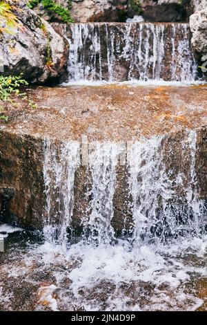 Wasser fließt über die Felsen, ein Wasserfall im Garten. Vertikales Foto. Stockfoto
