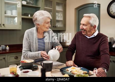 Du bist mein Lieblingstee. Ein liebevolles Seniorenpaar trinkt Tee und iß zusammen in der Küche zu Hause. Stockfoto