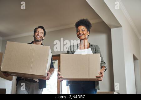 Ein junges Paar lächelt, während sie Kisten in ihr neues Zuhause trägt. Stockfoto