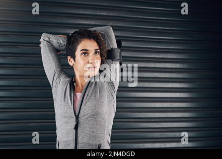 Spüren Sie das Summen der Fitness. Eine junge Frau macht einige Aufwärmstrecken, bevor sie draußen vor einem schwarzen Hintergrund trainiert. Stockfoto