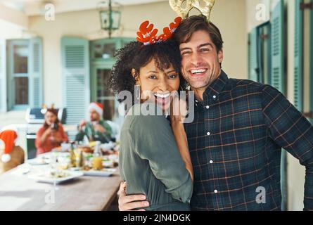 Verbringen Sie Weihnachten mit den Menschen, die Sie lieben. Portrait eines glücklichen jungen Paares, das gemeinsam mit Freunden und Familie beim Mittagessen Weihnachten feiert Stockfoto
