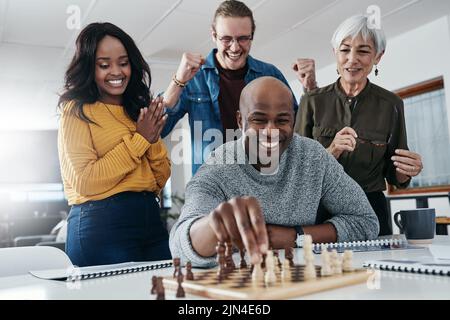 Es gibt einen Grund, warum hes unseren Champion, er gewinnt immer. Ein reifer Geschäftsmann spielen Schach in seinem Büro mit seinen Kollegen verwurzelten und beobachten in der Stockfoto