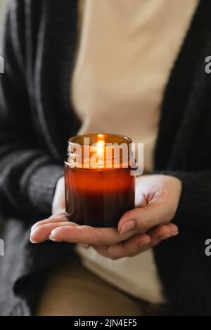 Frau hält in der Hand brennende Kerze in einem kleinen Glas Bernstein mit Holzdocht. Zen- und Relax-Konzept. Stockfoto