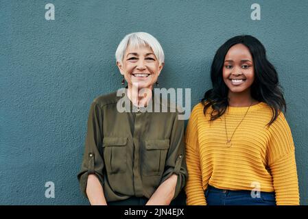 Wurden für den Erfolg zusammen gestellt. Porträt einer fröhlichen reifen und jungen Geschäftsfrau, die sich im Freien an einer Wand posiert. Stockfoto