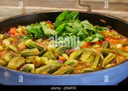 Okra und gebratene lila Zwiebeln werden mit Koriander und Basilikum auf dem Gasherd in der Pfanne gebraten Stockfoto