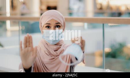 Junge Frau in medizinischer Schutzmaske zeigt mit Handflächen-Stop-Zeichen Geste Verbot der Annäherung wegen Pandemie Ausbruch bietet an, ein Atemschutzgerät zu setzen Stockfoto