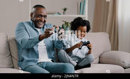 Glückliche afroamerikanische Familie Vater und Tochter haben Spaß zusammen Vater spielen Videospiel auf der Konsole mit Kind Mädchen verwenden Controller sitzen auf der Couch Stockfoto
