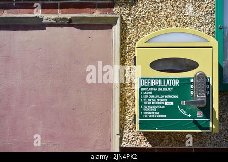 Öffentlicher Defibrillator, der an einer Gebäudewand für den Notfall mit vollständigen Anweisungen montiert ist. Stockfoto