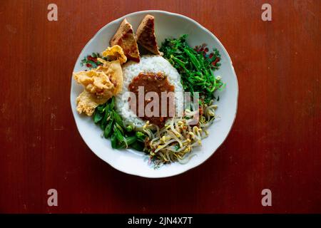 Nasi Pecel oder sego Pecel ist ein traditionelles javanesisches Reisgericht aus gedünstetem Reis mit Gemüsesalat, Erdnusssauce, Tempeh, Tofu-Bohnensprossen und Crackern Stockfoto