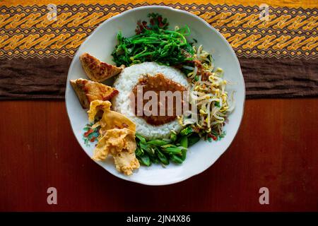 Nasi Pecel oder sego Pecel ist ein traditionelles javanesisches Reisgericht aus gedünstetem Reis mit Gemüsesalat, Erdnusssauce, Tempeh, Tofu-Bohnensprossen und Crackern Stockfoto