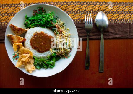 Nasi Pecel oder sego Pecel ist ein traditionelles javanesisches Reisgericht aus gedünstetem Reis mit Gemüsesalat, Erdnusssauce, Tempeh, Tofu-Bohnensprossen und Crackern Stockfoto