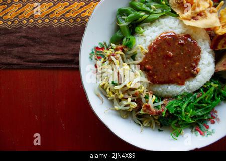 Nasi Pecel oder sego Pecel ist ein traditionelles javanesisches Reisgericht aus gedünstetem Reis mit Gemüsesalat, Erdnusssauce, Tempeh, Tofu-Bohnensprossen und Crackern Stockfoto