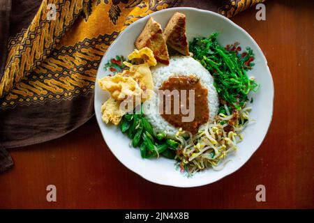 Nasi Pecel oder sego Pecel ist ein traditionelles javanesisches Reisgericht aus gedünstetem Reis mit Gemüsesalat, Erdnusssauce, Tempeh, Tofu-Bohnensprossen und Crackern Stockfoto