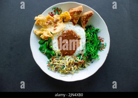 Nasi Pecel oder sego Pecel ist ein traditionelles javanesisches Reisgericht aus gedünstetem Reis mit Gemüsesalat, Erdnusssauce, Tempeh, Tofu-Bohnensprossen und Crackern Stockfoto