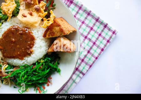 Nasi Pecel oder sego Pecel ist ein traditionelles javanesisches Reisgericht aus gedünstetem Reis mit Gemüsesalat, Erdnusssauce, Tempeh, Tofu-Bohnensprossen und Crackern Stockfoto