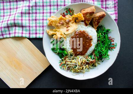 Nasi Pecel oder sego Pecel ist ein traditionelles javanesisches Reisgericht aus gedünstetem Reis mit Gemüsesalat, Erdnusssauce, Tempeh, Tofu-Bohnensprossen und Crackern Stockfoto