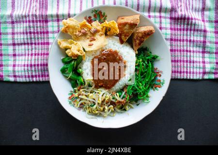 Nasi Pecel oder sego Pecel ist ein traditionelles javanesisches Reisgericht aus gedünstetem Reis mit Gemüsesalat, Erdnusssauce, Tempeh, Tofu-Bohnensprossen und Crackern Stockfoto